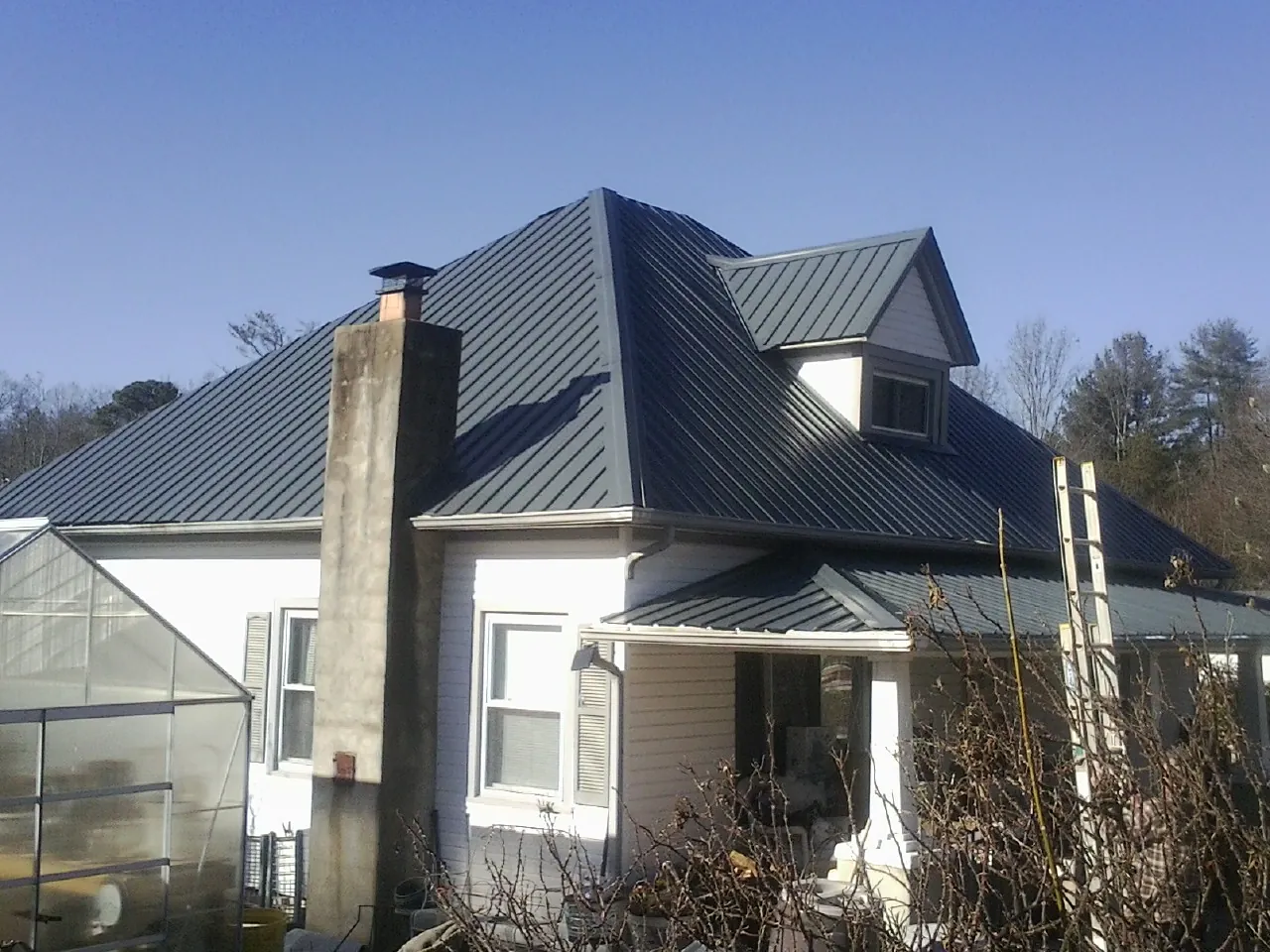 Dark blue standing seam metal roof on a white farmhouse with dormer — Slate & Tile Roof Repair by Roofing Brothers in Falls Of Rough