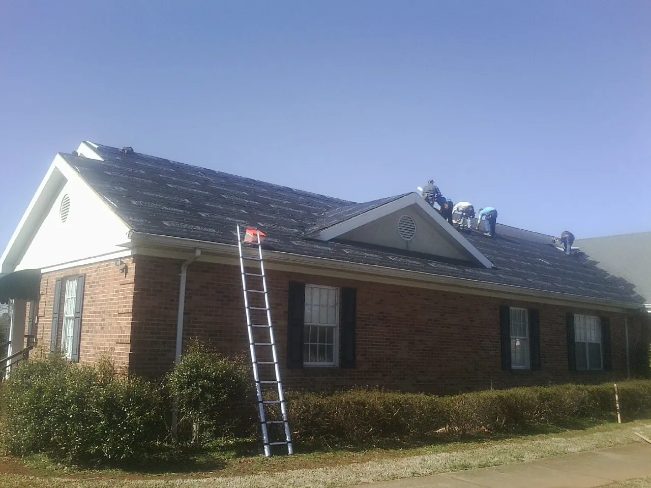 Crew tearing shingles off a brick ranch roof with a ladder set — Emergency Roof Repair work by our crew in Falls Of Rough