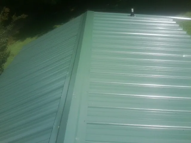 New green metal panels meeting at the ridge of a roof — Flat Roof Repair work by our crew in Falls Of Rough