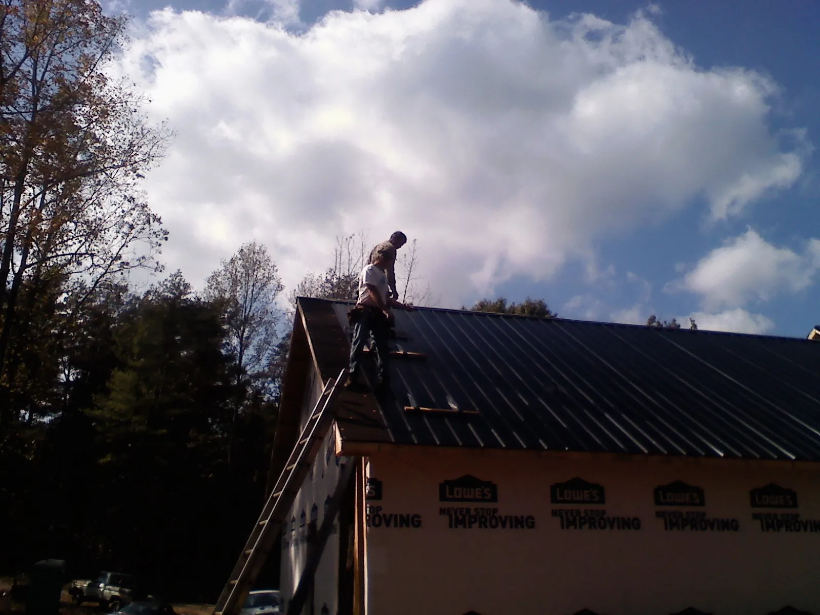 Roofer fastening dark metal panels high against a cloudy sky, from a Roof Inspection job in Falls Of Rough