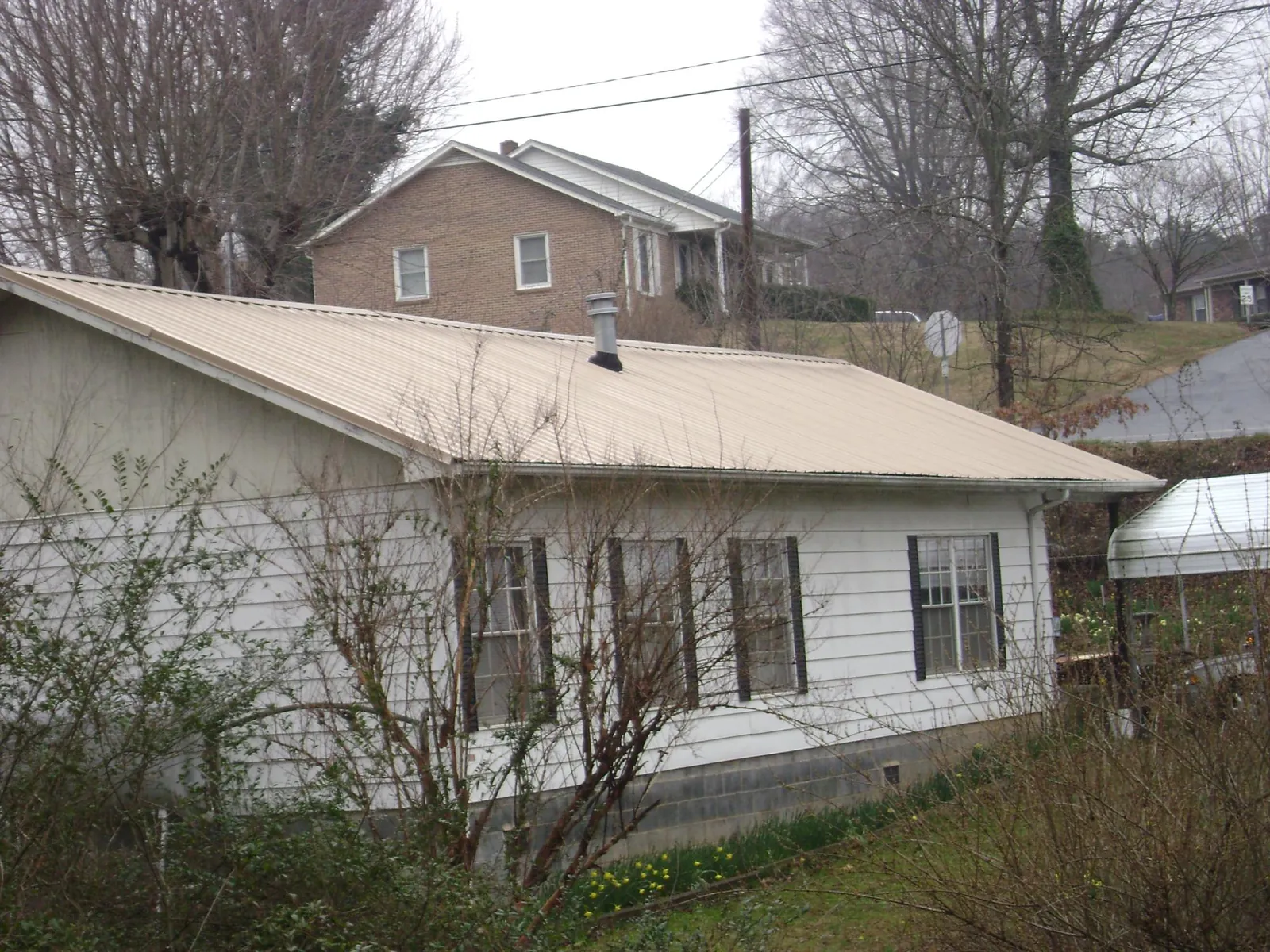 Tan metal roof on a white sided house set into a hillside — Commercial Roofing by Roofing Brothers in Falls Of Rough