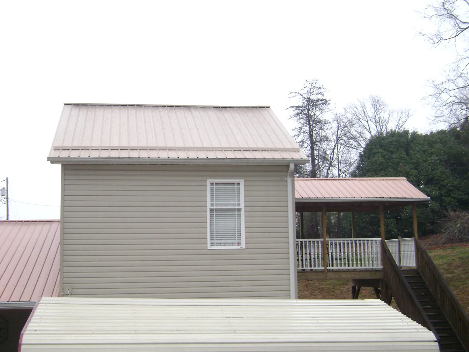 Tan metal roofs on a two story addition and attached porch, from a Roof Replacement job in Falls Of Rough
